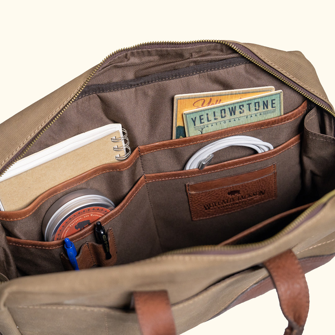Canvas bag with leather straps and metal fastenings, emphasizing craftsmanship and rugged design.