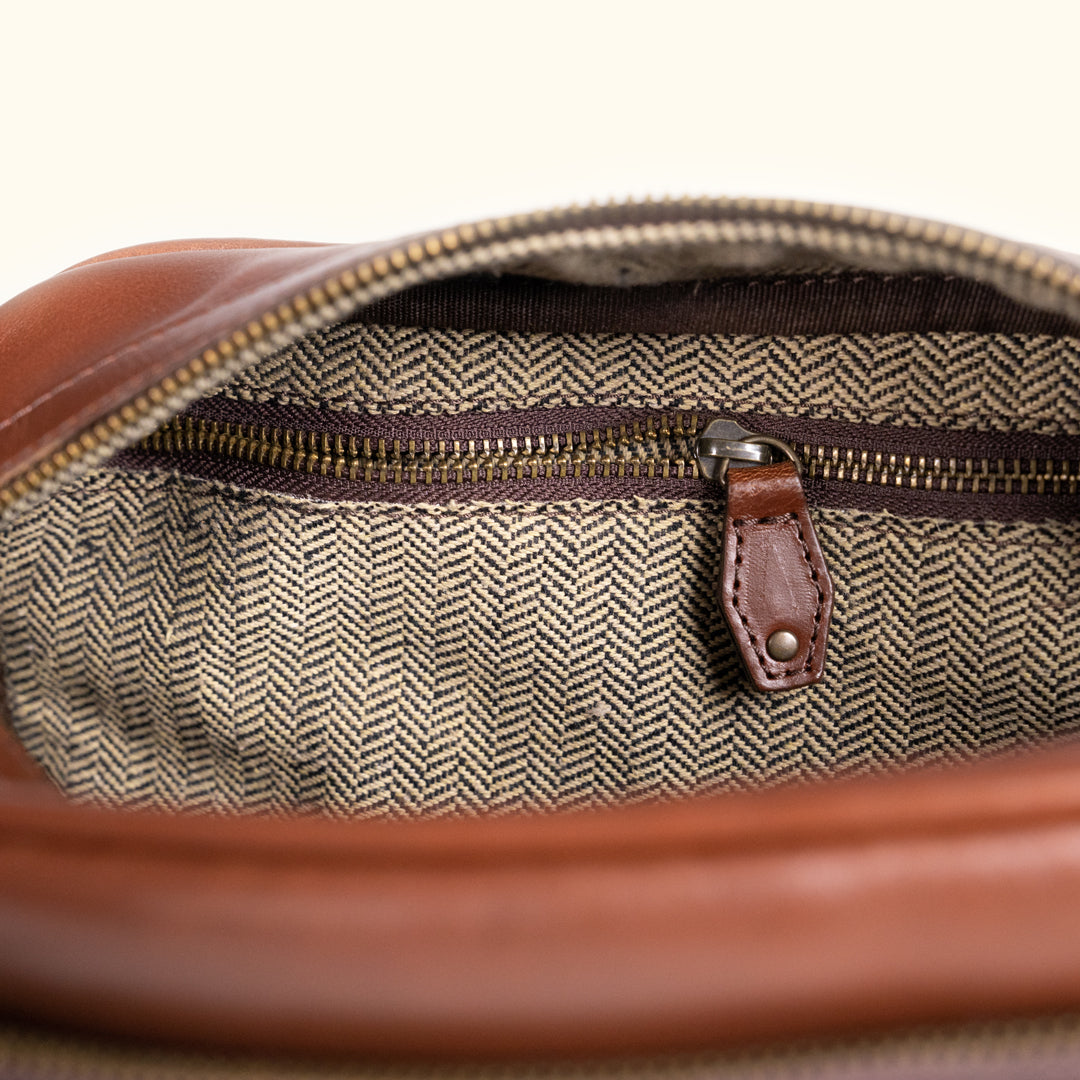 Interior view of a brown leather bag, highlighting its elegant herringbone pattern and zippered pocket.