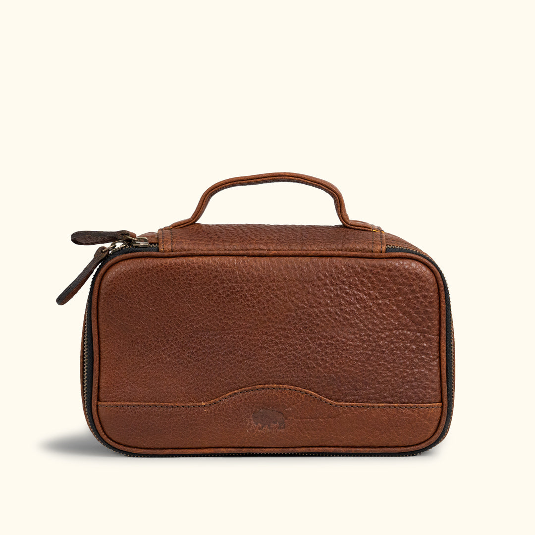 Luxurious brown leather travel pouch with finely stitched detailing, twin zipper pulls, and a solid top handle for sophisticated travelers.