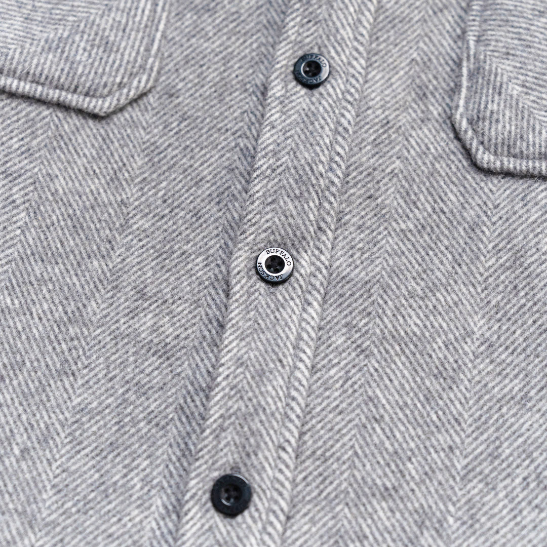Close-up of a gray herringbone fabric garment with a button placket and dark buttons.