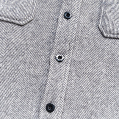 Close-up of a gray herringbone fabric garment with a button placket and dark buttons.