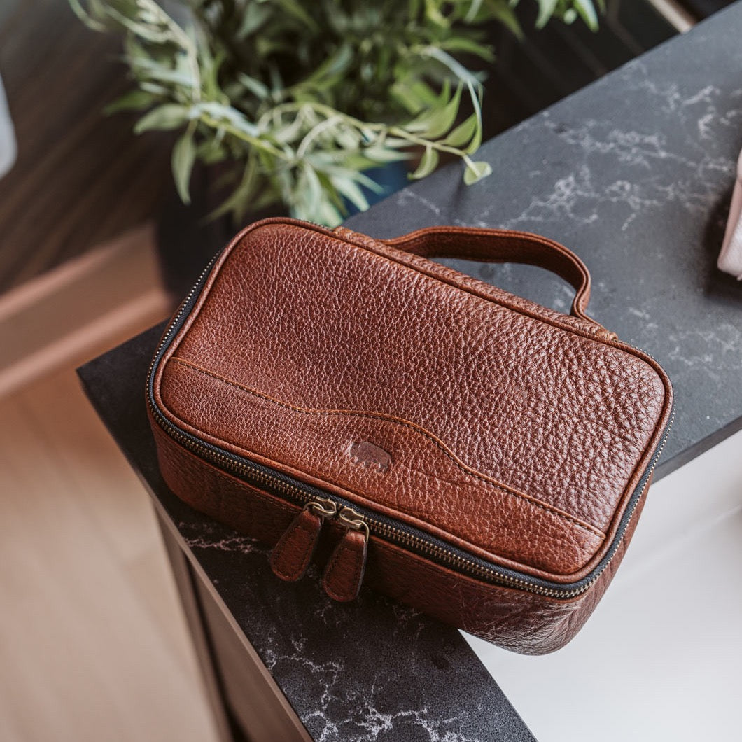 Rich brown leather dopp kit placed on a dark marble countertop, partially open to reveal a well-organized interior ideal for sophisticated travel.