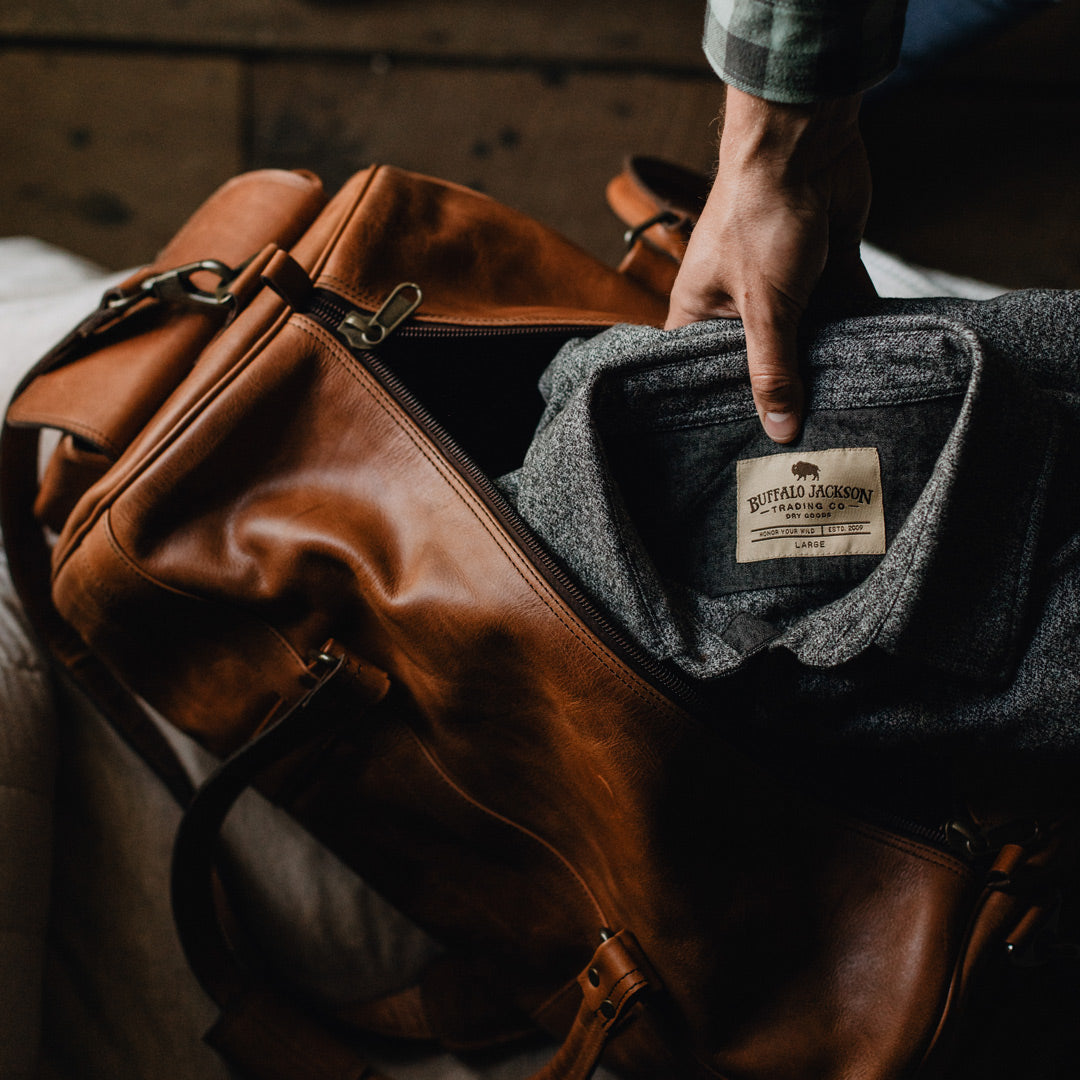 Roosevelt Buffalo Leather Duffle Bag in Autumn Brown, unzipped to reveal gray button-up shirt, robust build, practical for stylish travel.