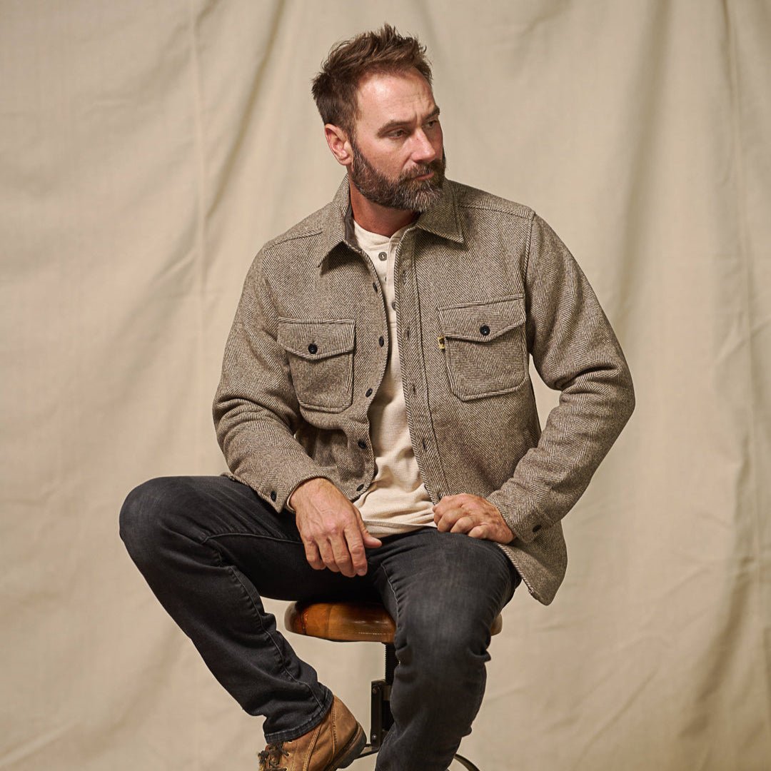 Man seated wearing the Riverton Wool Shirt Jac in Ashen Brown over a cream henley with dark jeans