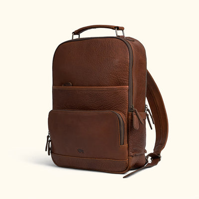 A brown full grain leather backpack with multiple compartments and a cushioned shoulder strap pad