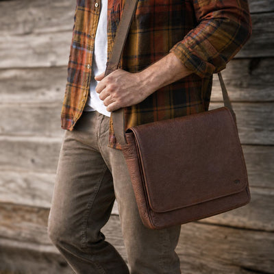 Person wearing a plaid shirt and holding a brown leather bag on a wooden staircase.