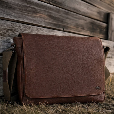 Brown leather bag leaning against a wooden wall.