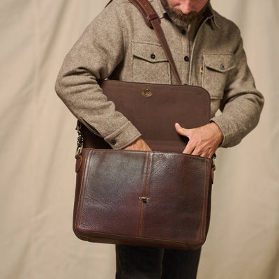 Man carrying the Roosevelt Leather Messenger Bag by the cushioned top handle — Full Single Flap Buffalo Grain full-grain leather with antique brass hardware