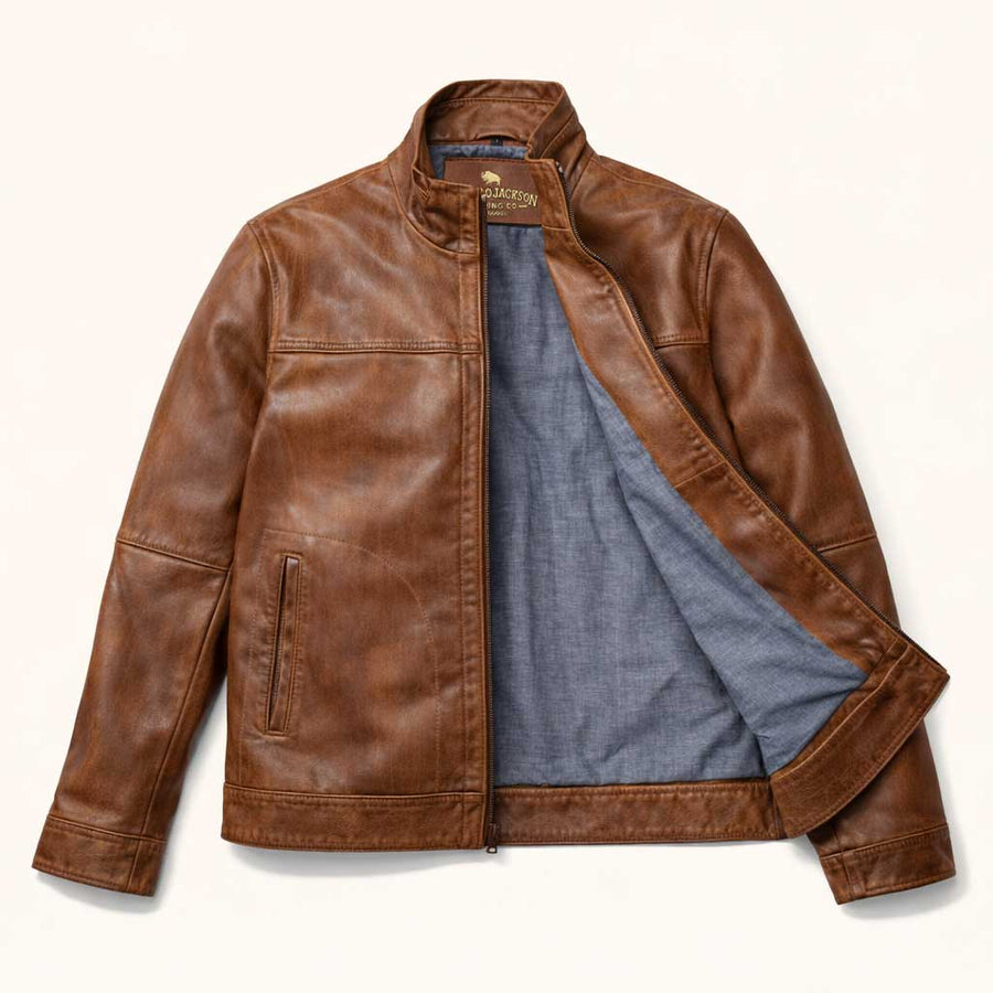 Man wearing a brown leather jacket sitting on a wooden stool against a beige background