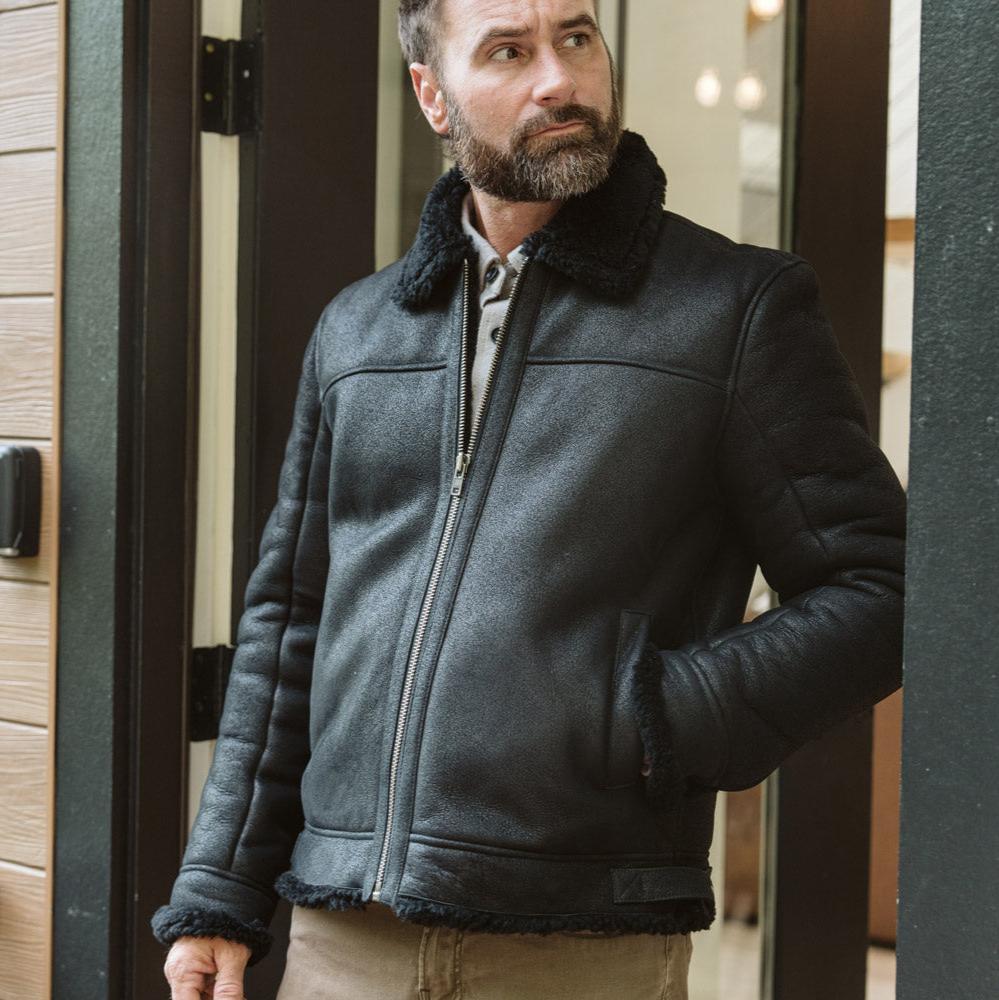 Black shearling leather bomber jacket hanging at a cabin