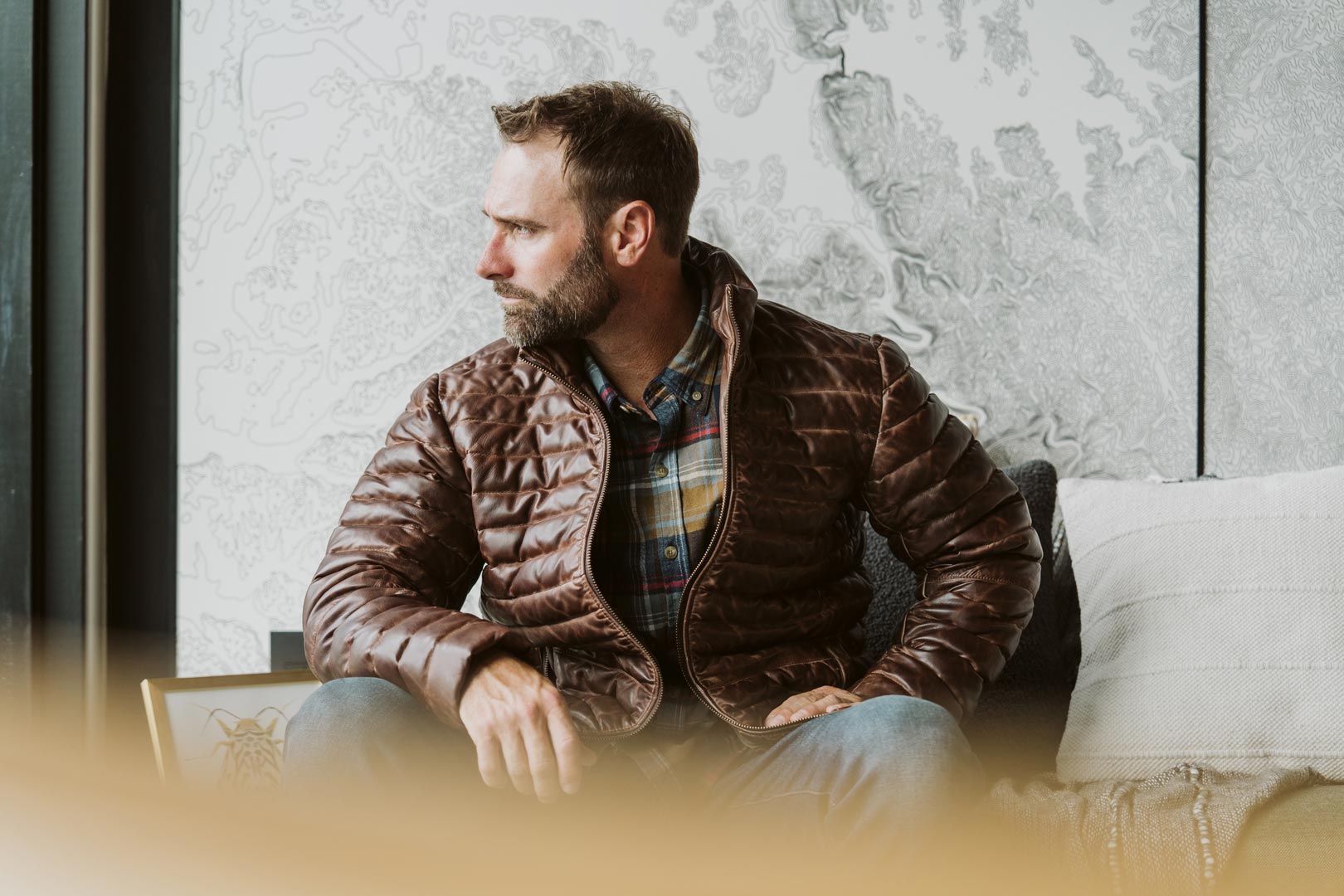 Bearded man in a brown puffer jacket, seated and gazing out the window, exuding a relaxed vibe.