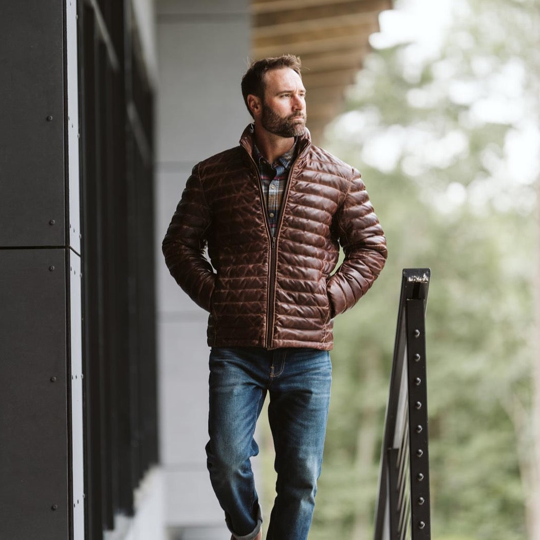 Outdoorsman dressed in a brown puffer jacket and plaid shirt, walking and looking pensive.
