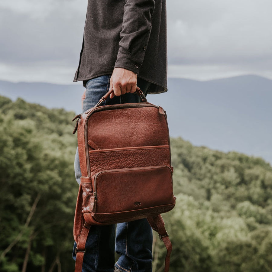 A brown full grain leather backpack with multiple compartments and a cushioned shoulder strap pad