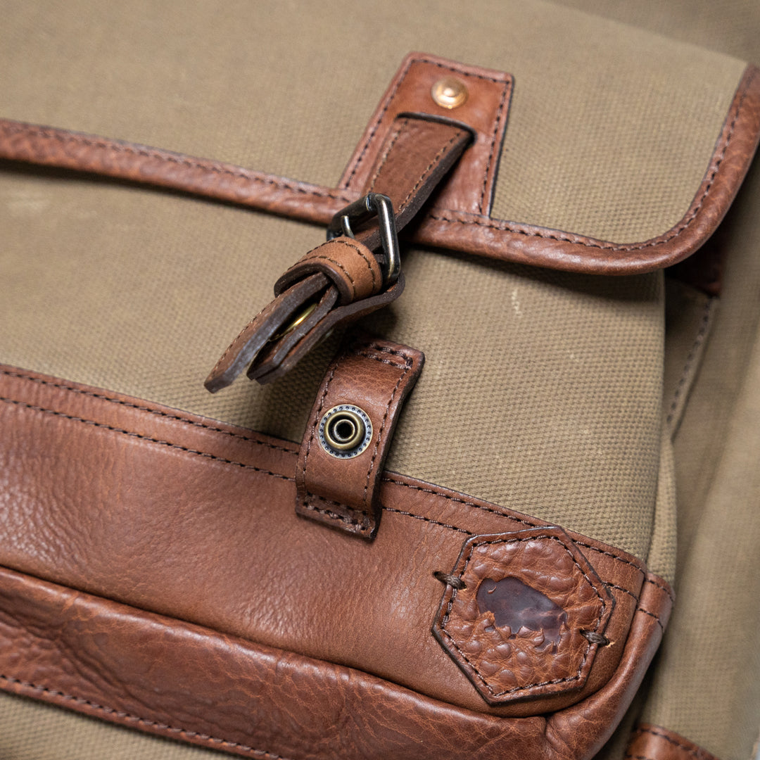 Close-up of a bag's leather buckle and canvas material, showcasing quality stitching and hardware.