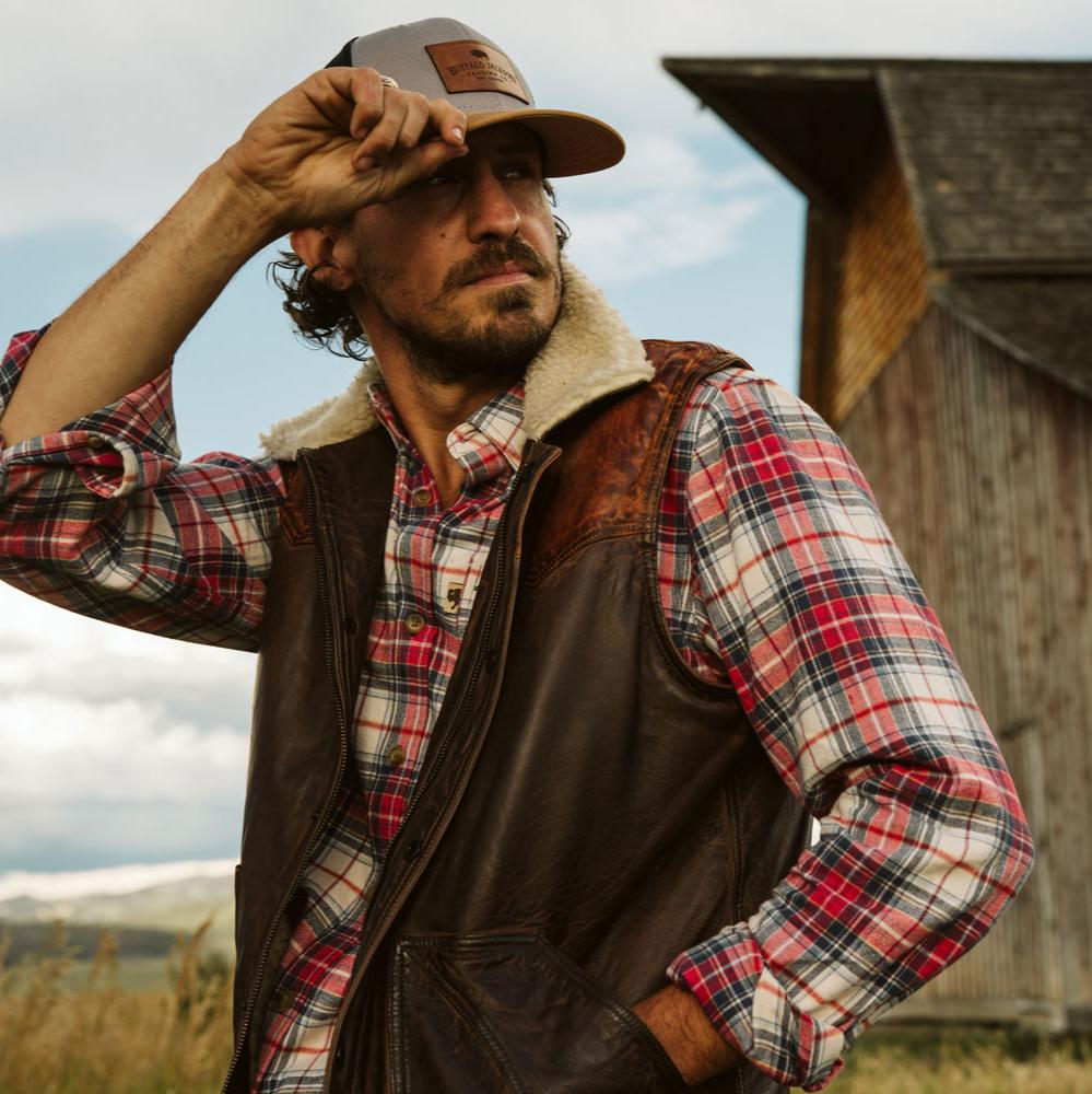 Man in a cap wearing the Jackson Leather Sherpa Vest over a red plaid flannel
