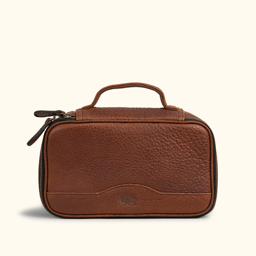 Compact brown leather dopp kit with textured finish, sturdy handle, and dual zipper pulls, perfect for organized travel essentials.