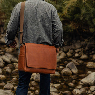 Person with a brown leather bag walking along a rocky path with greenery.