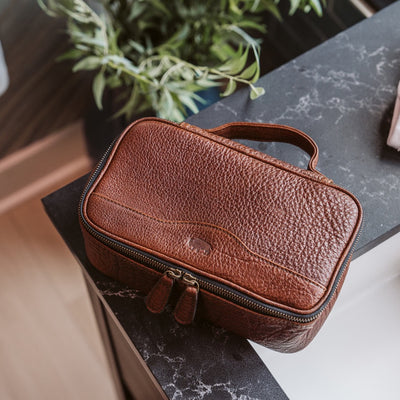 Rich brown leather dopp kit placed on a dark marble countertop, partially open to reveal a well-organized interior ideal for sophisticated travel.