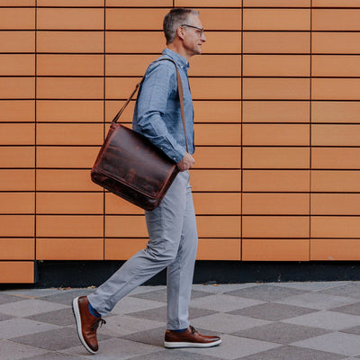 Sleek dark oak leather satchel messenger bag carried by a man in urban attire, featuring a polished finish and spacious design.