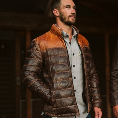Man wearing a brown leather puffer jacket with a contrasting collar, standing outdoors with a confident expression.