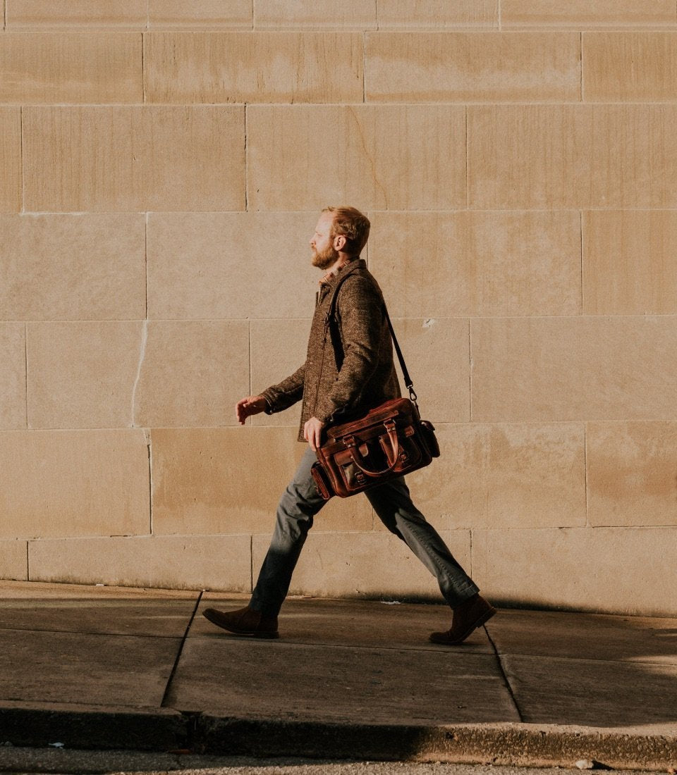 Man walking with the Roosevelt Buffalo Leather Pilot Bag in Dark Oak carried by its top handles